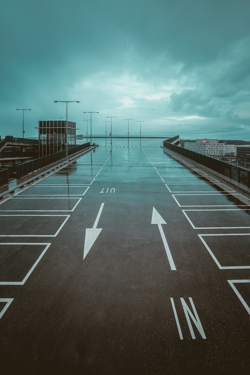 Parking extérieur vide et mouillé sur un toit, avec des lignes blanches et des lampadaires.