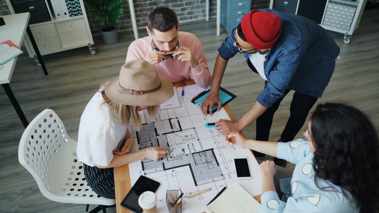Des professionnels collaborent sur un plan d'étage architectural à une table.