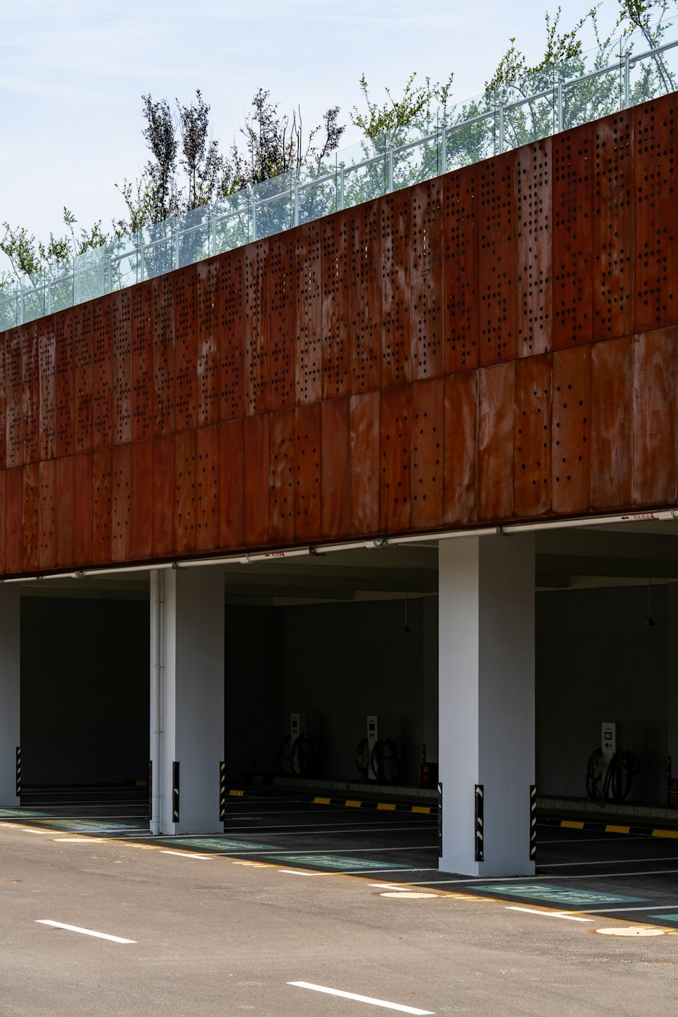 Parking moderne avec façade en métal rouillé et bornes de recharge.