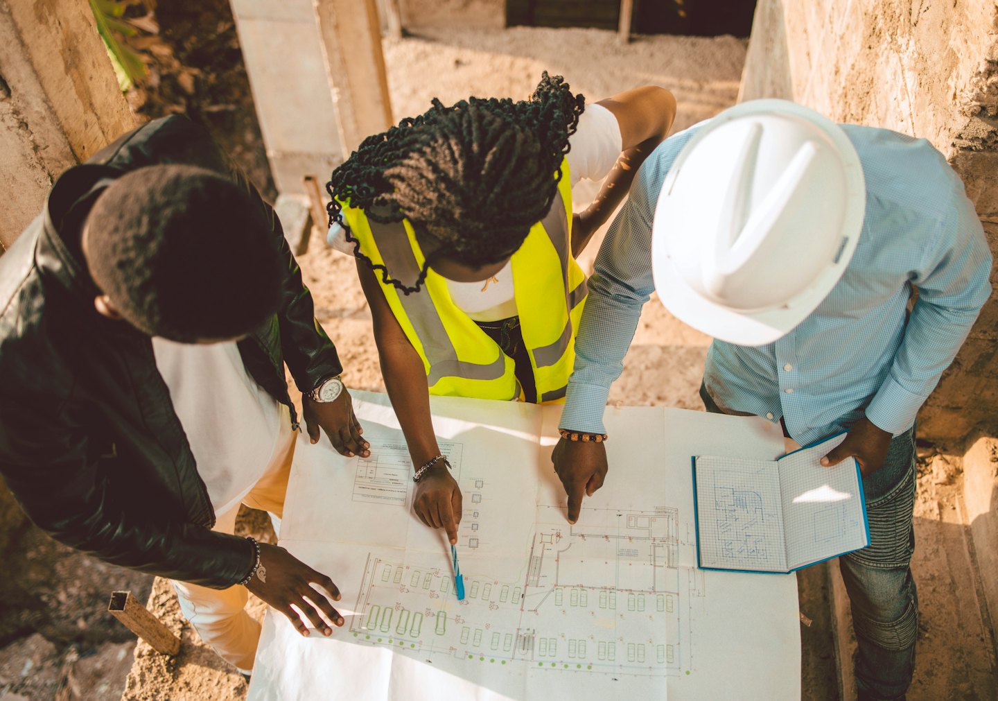 Trois professionnels de la construction examinent des plans sur un chantier en béton.